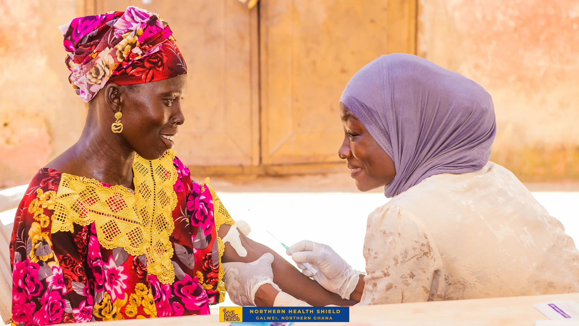 A smiling woman receives a vaccination at a Northern Health Shield outreach in Galwei, Northern Ghana