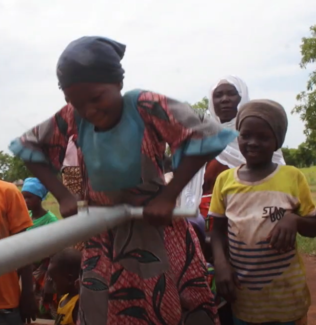 child pumping water from a borehole Give Basic Needs installed in a village in Ghana