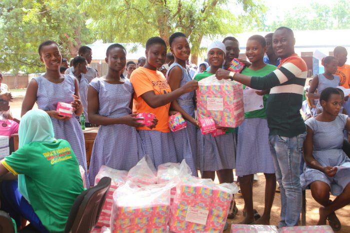 smiling girls standing outside holding pads at a giving event by give basic needs
